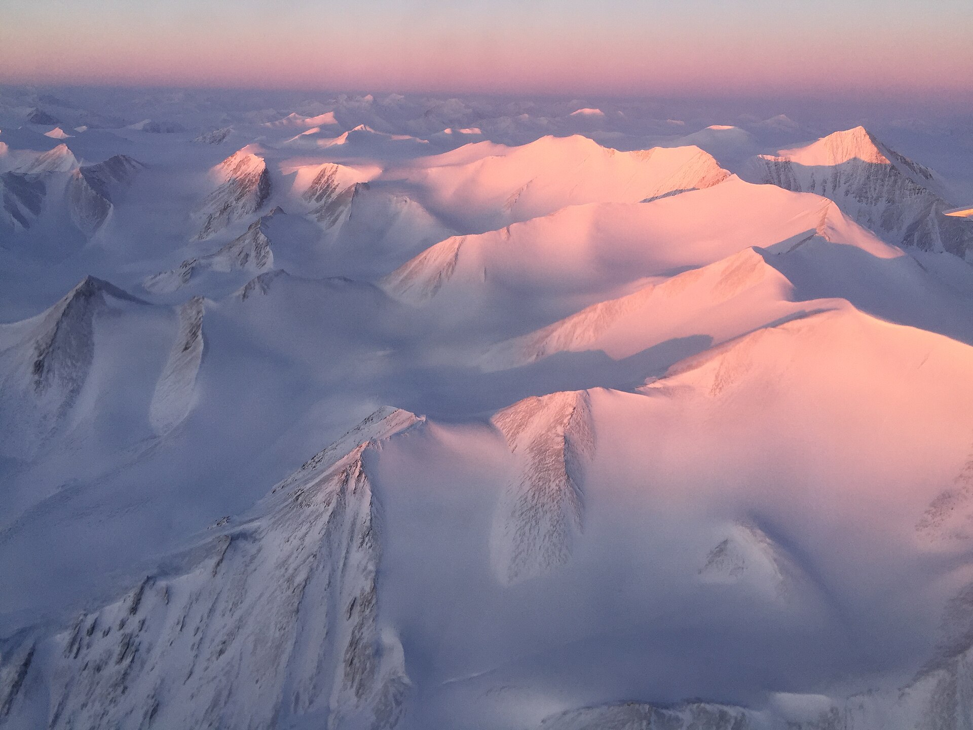 Snow-covered mountain peaks of Ellesmere Island catching the first sunlight, seen from an aircraft