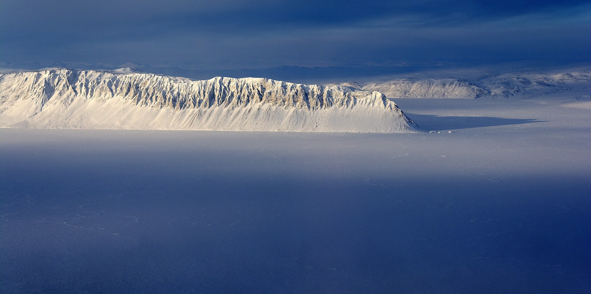 Aerial view of a frozen sound between dark, snow-streaked mountains in the High Arctic